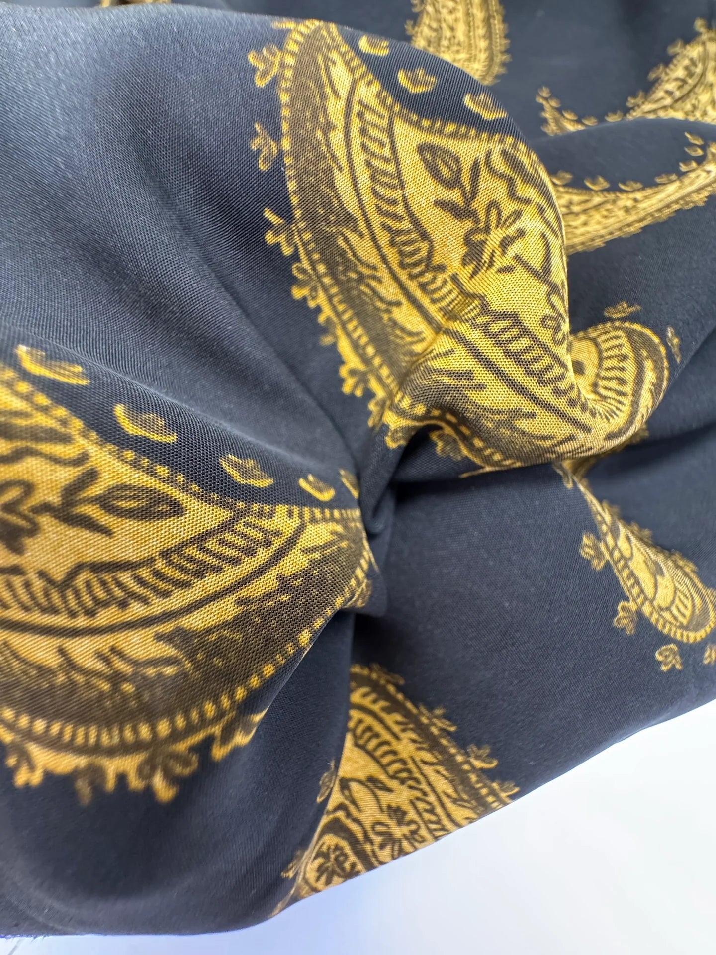 Attēls ar Itālijas 100% viskozes šifona audums ar zeltainu paisley rakstu uz melna fona – pieejams internetā Šarlotes audumi